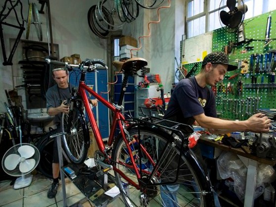 Two men working in a Bicycle repair shop, with tools of the trade.